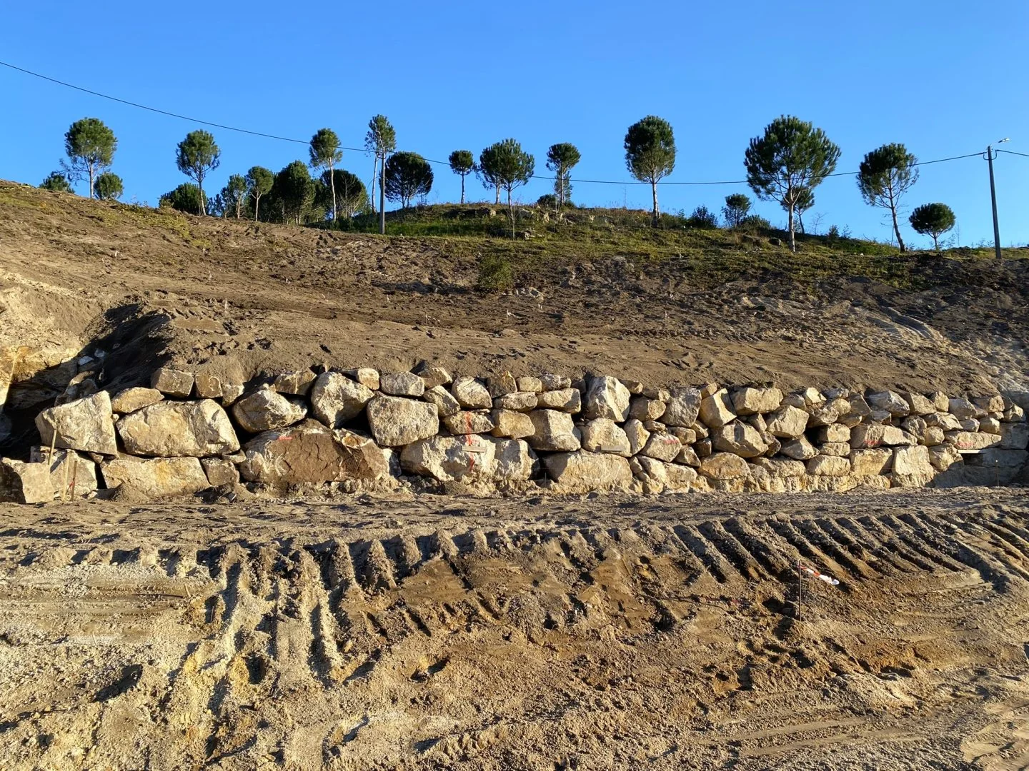 Muro de blocos de granito e talude modelado, com as árvores plantadas na crista.